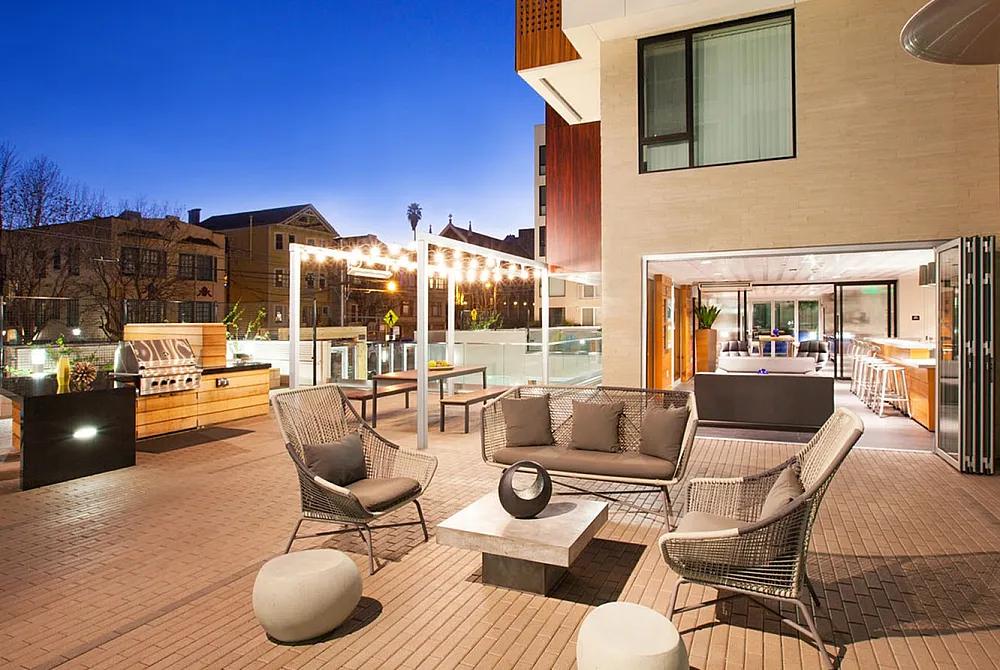 Elegant apartment outdoor patio at sunset, featuring modern seating, ambient lighting, and a barbecue area.