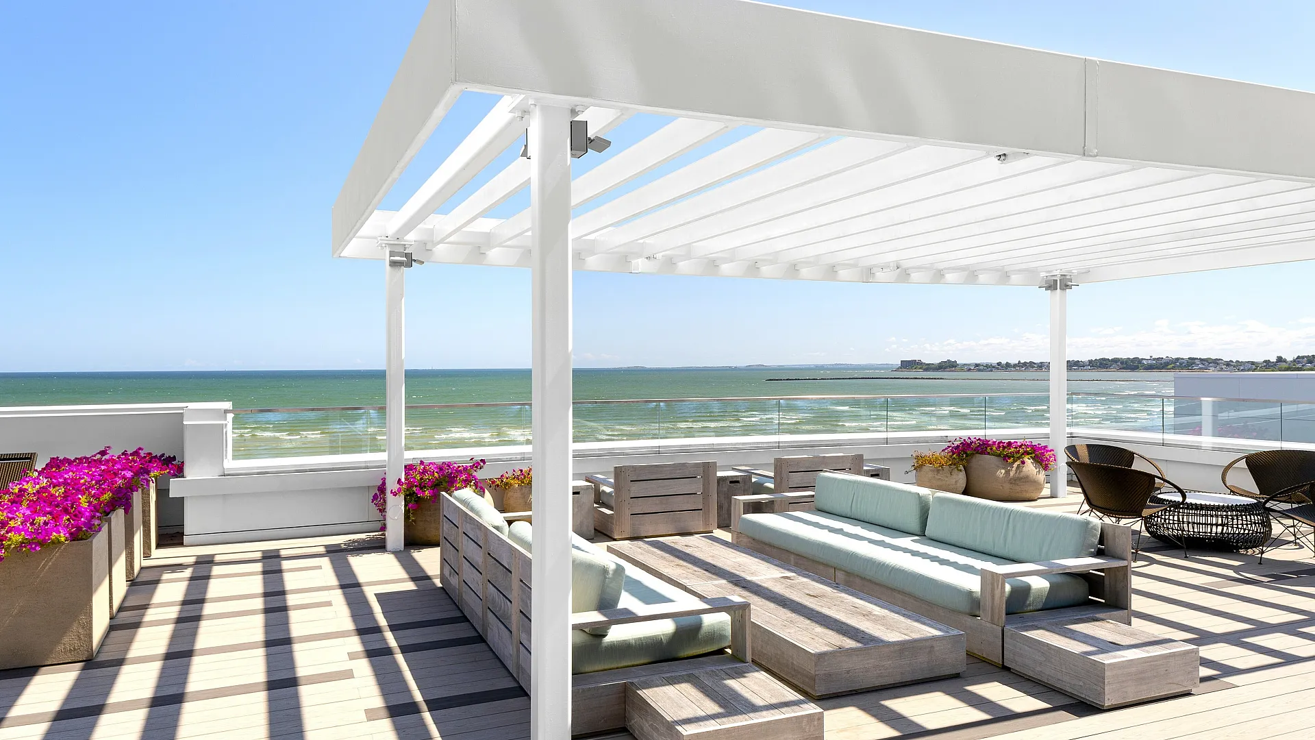 Luxurious rooftop deck with ocean view, featuring elegant seating under a modern pergola, flanked by vibrant flower arrangements.