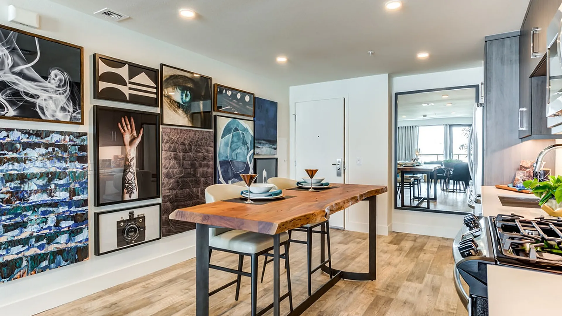 Modern kitchen area with artistic wall gallery, stylish wooden dining table, and sleek appliances, offering a chic and inviting atmosphere.