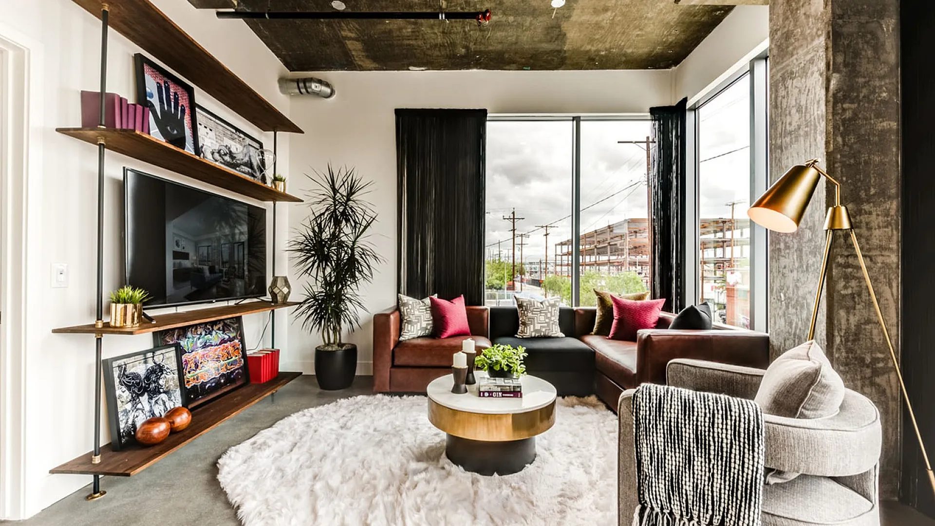 Chic urban living room with modern decor, featuring a large L-shaped sofa, stylish armchair, and a contemporary floor lamp. Bright and inviting space with floor-to-ceiling windows and trendy shelving.