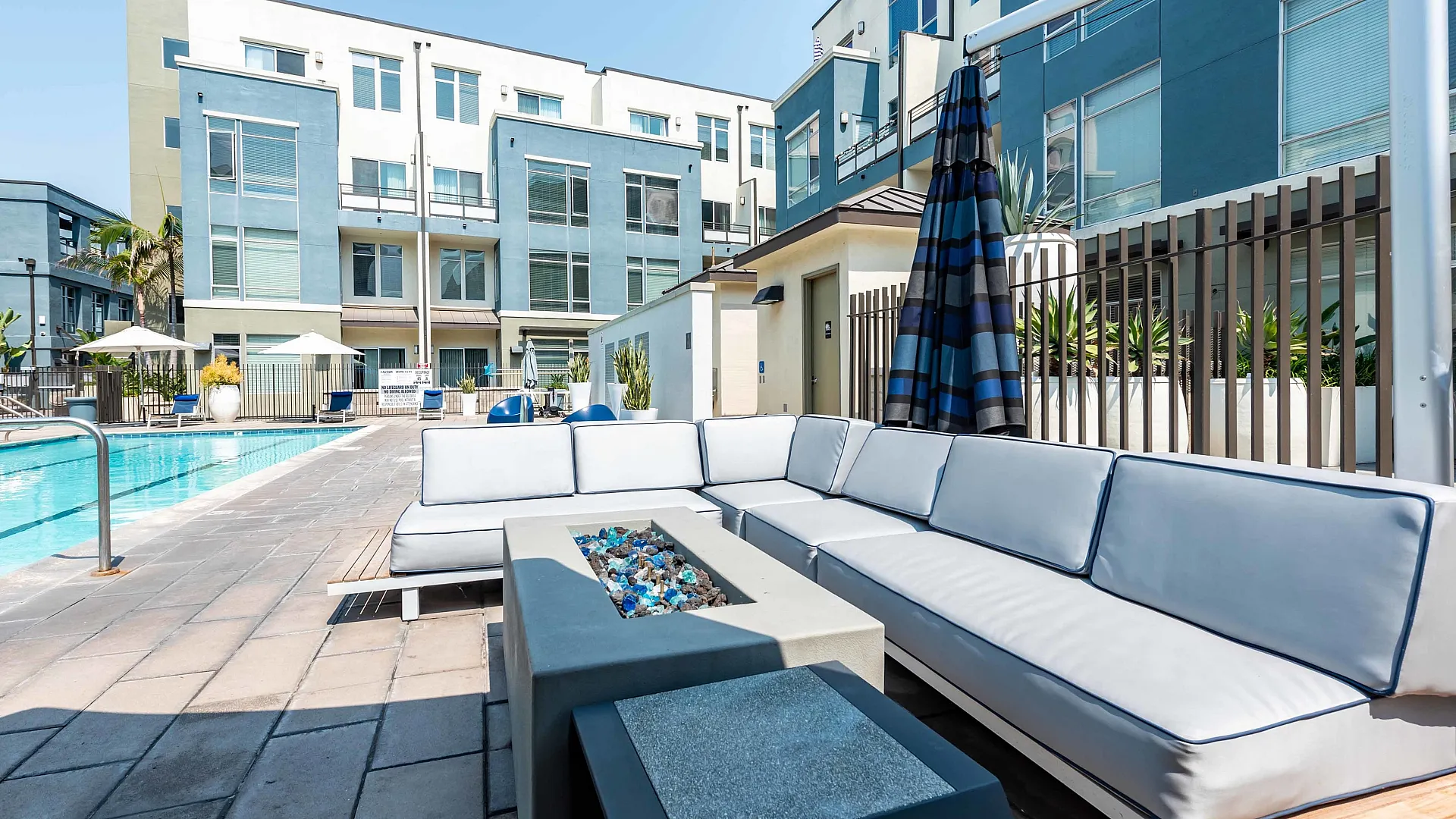 Modern apartment complex with a luxurious outdoor pool area featuring elegant white seating and a contemporary fire pit, perfect for relaxation and social gatherings.