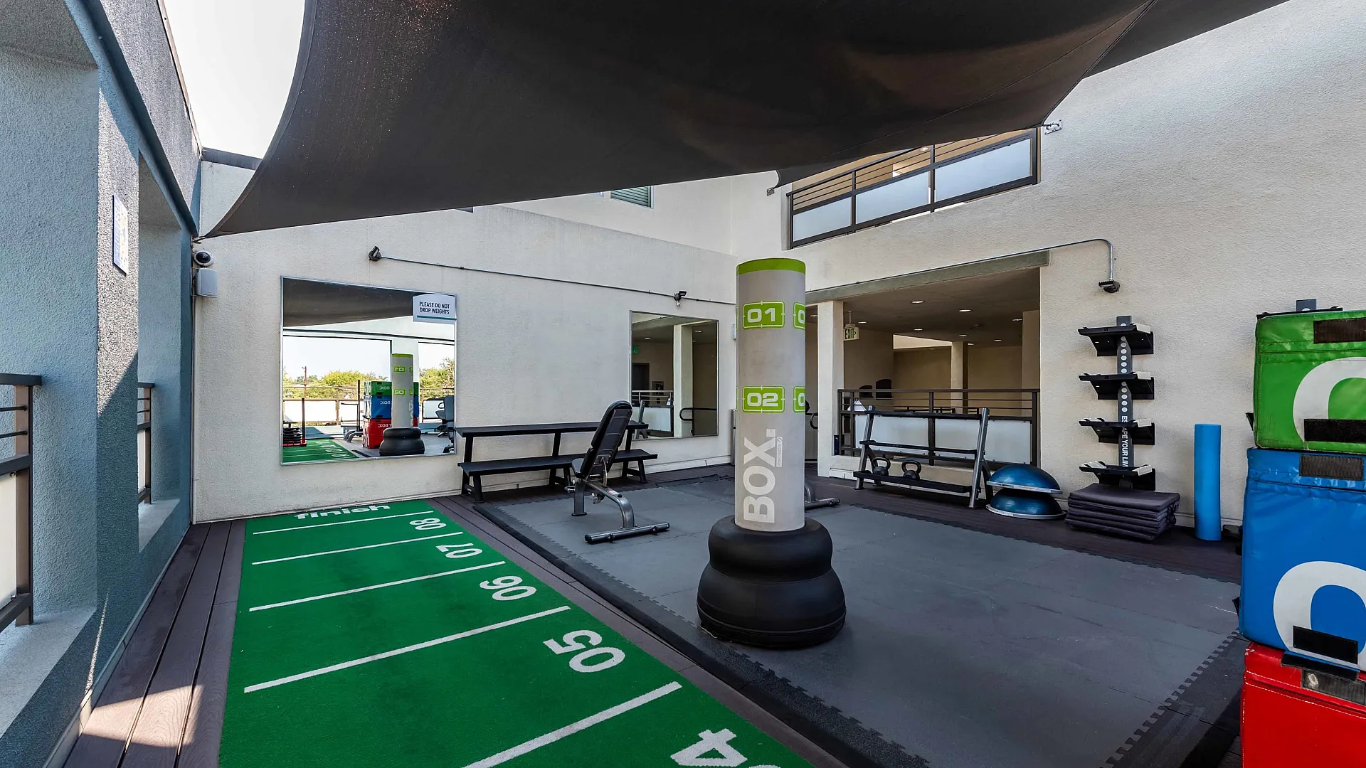 Modern outdoor gym area featuring a boxing bag, vibrant green track flooring, and various training equipment.