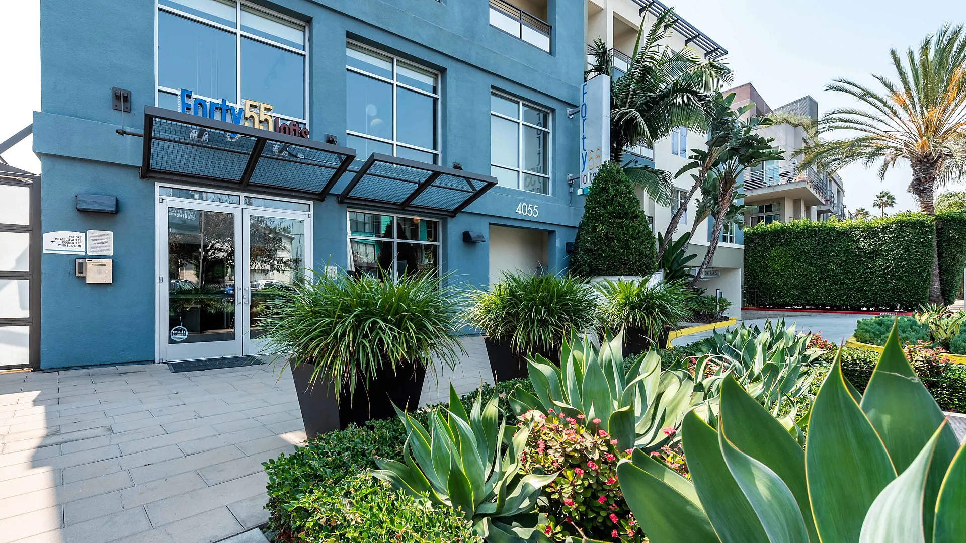 Modern apartment complex entrance with lush landscaping, vibrant greenery, and contemporary exterior design.