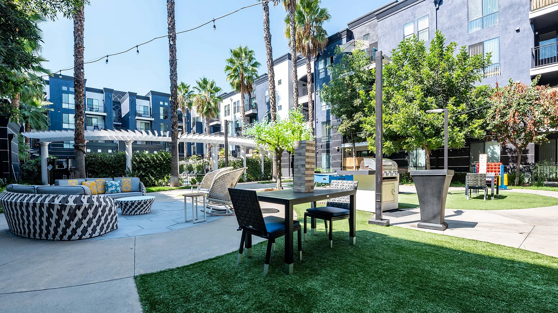 Chic apartment courtyard with lush landscaping, stylish seating areas, and convenient barbecue space under palm trees.