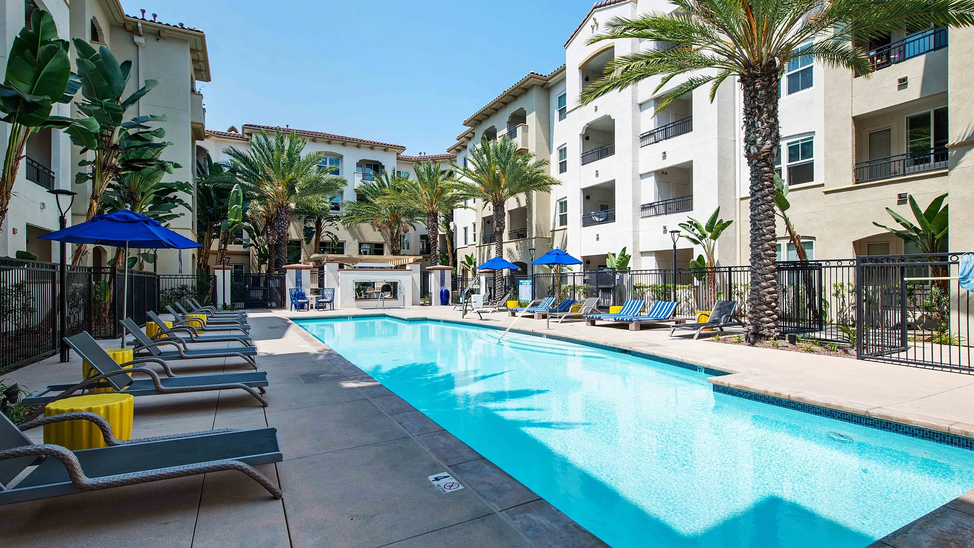 Luxurious apartment complex with a stunning swimming pool surrounded by palm trees and inviting sun loungers.