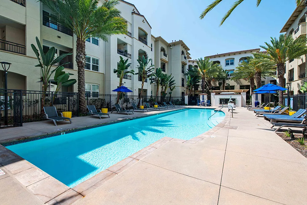 Luxurious apartment complex with a sparkling pool, surrounded by palm trees and stylish lounge chairs, perfect for relaxation.