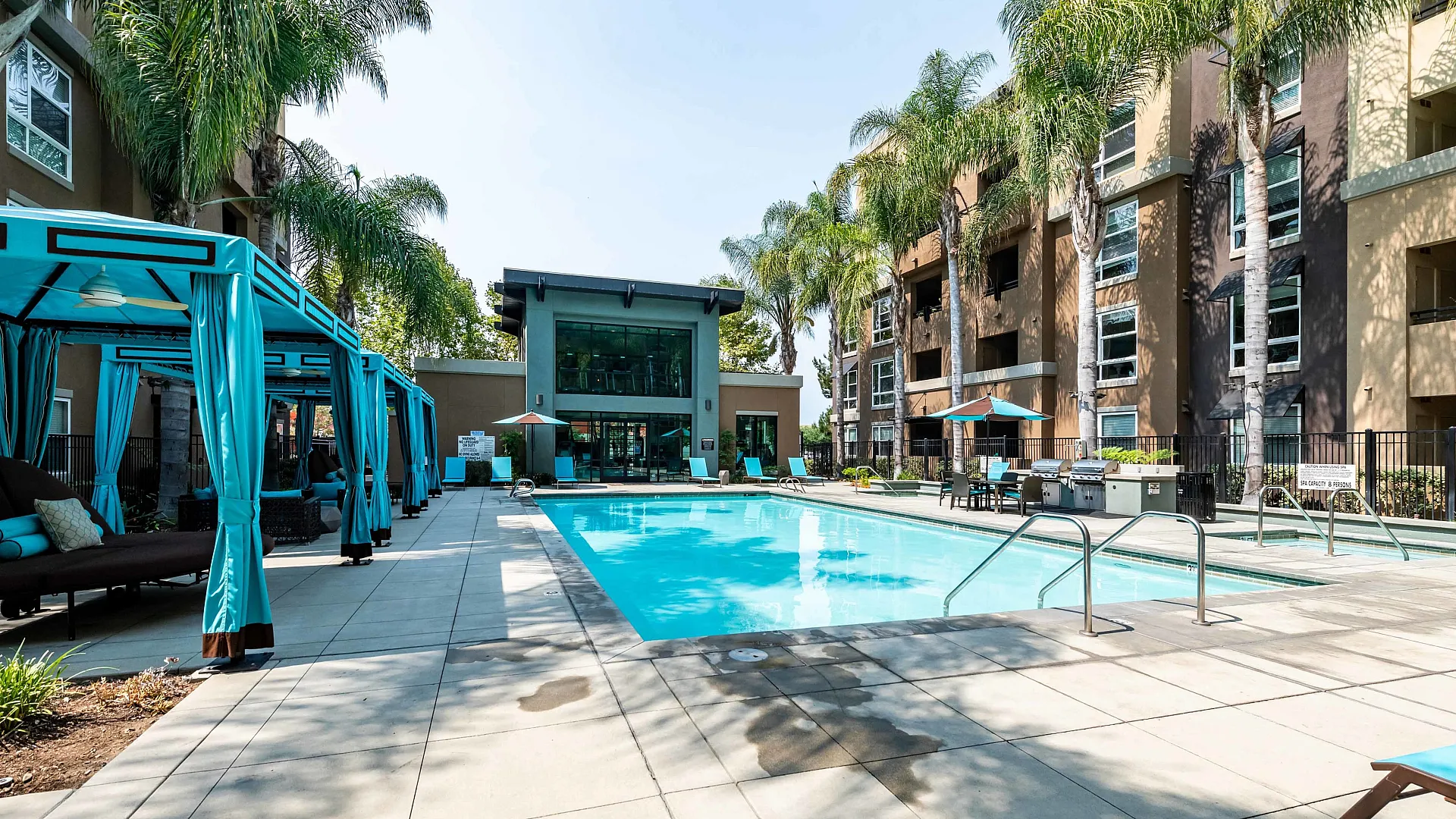 Luxurious apartment pool area with stylish cabanas and vibrant palm trees, perfect for relaxation and leisure.