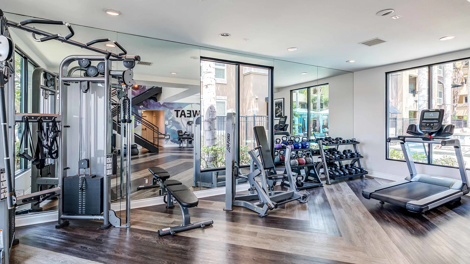Modern fitness center with state-of-the-art gym equipment, surrounded by large windows and stylish flooring.