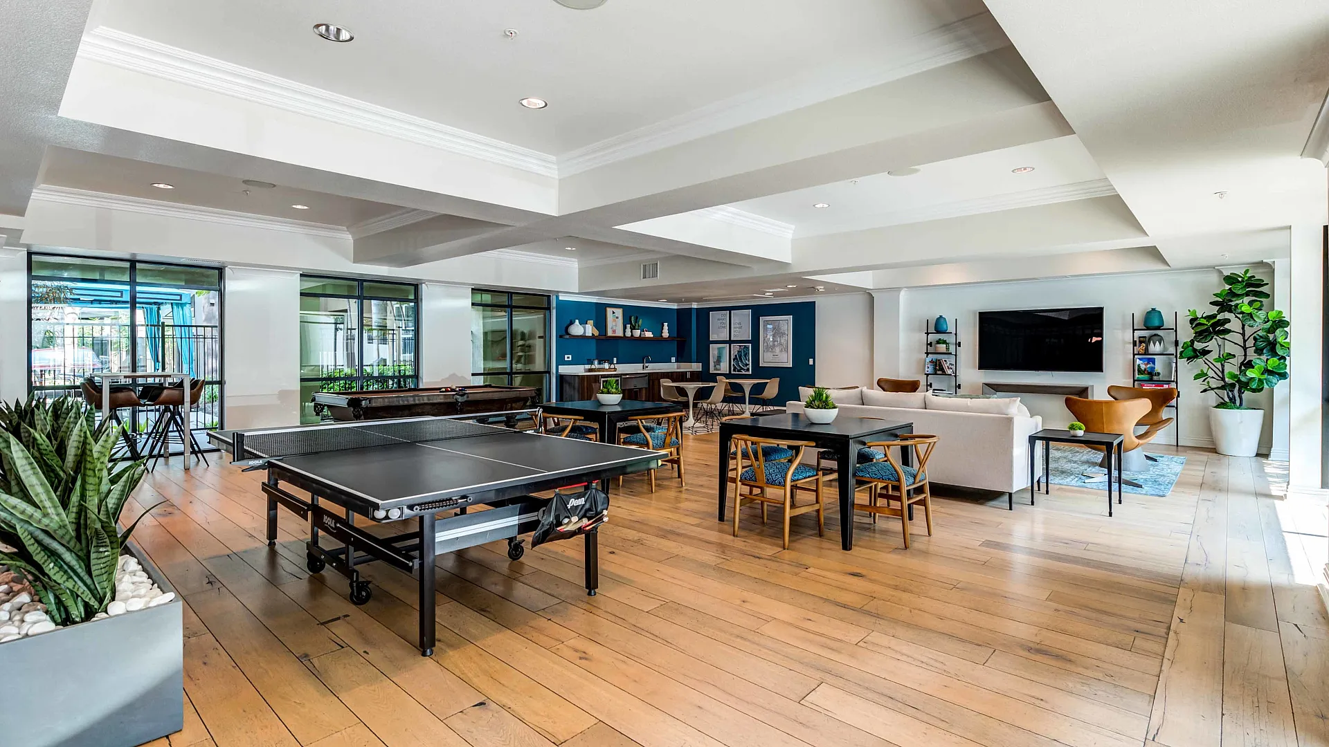 Modern and inviting community lounge featuring a sleek ping pong table, cozy seating area, and vibrant decor with natural light and greenery.