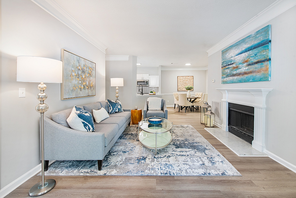 Elegant open-concept living room with modern decor, featuring a cozy gray sofa, decorative pillows, and a serene dining area in the background.