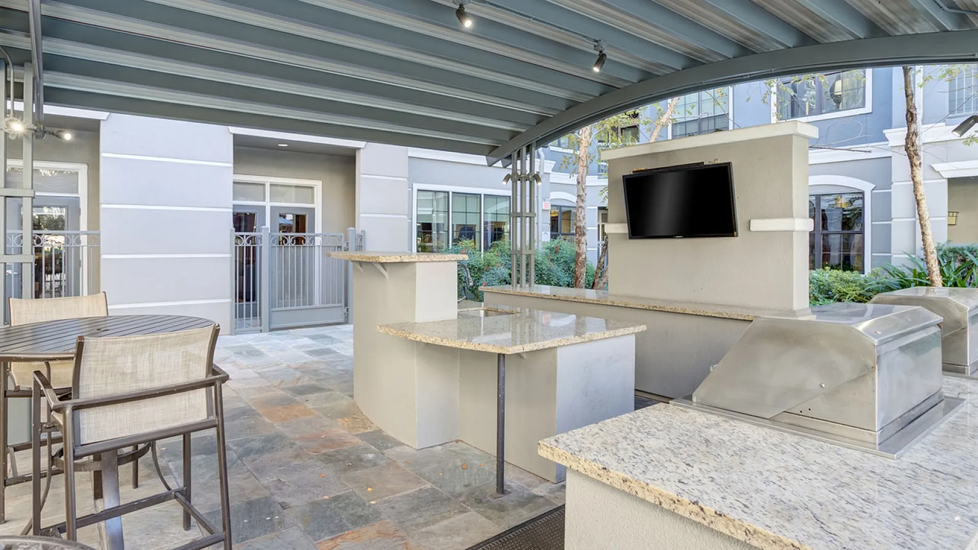 Elegant outdoor patio featuring a modern grill station, sleek granite countertops, and a mounted TV under a stylish pergola, offering a perfect spot for relaxation and entertainment.
