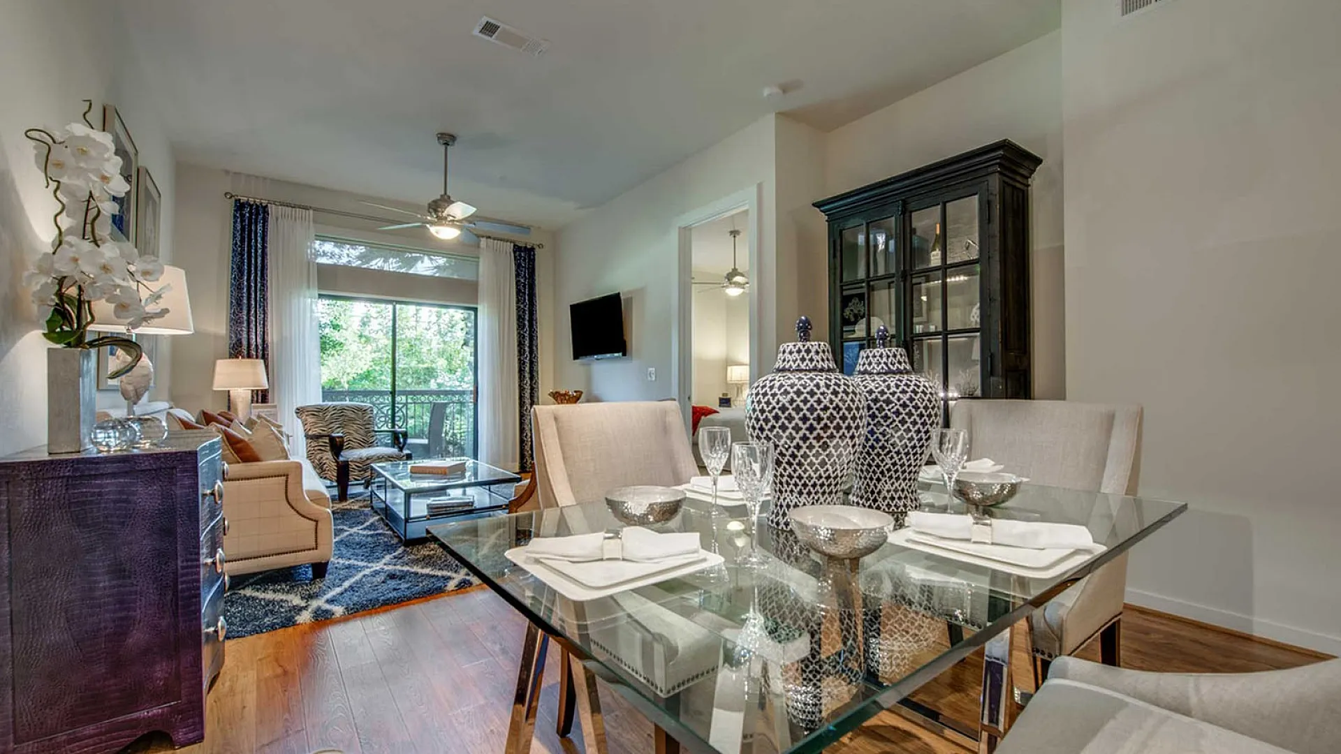 Elegant open-concept living room featuring a chic dining area with a glass table, stylish decor, and a scenic balcony view.