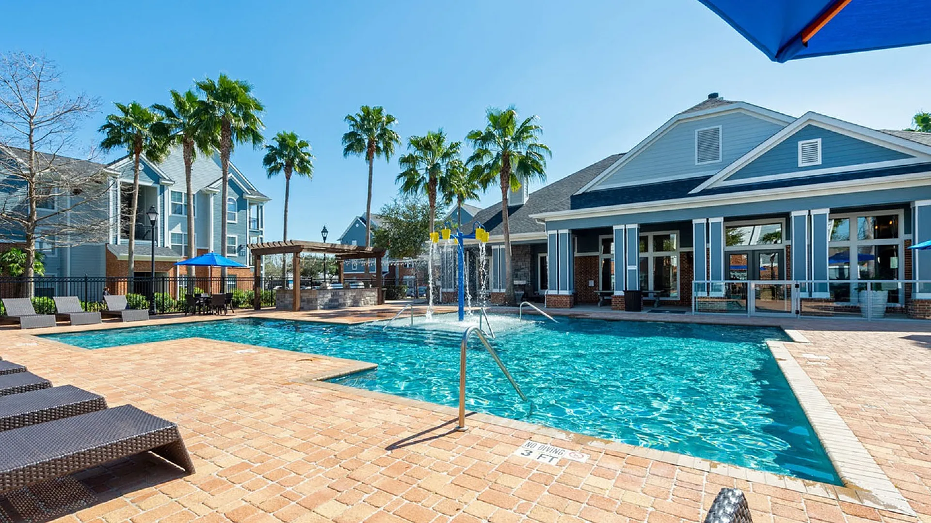 Inviting outdoor pool area with sleek sun loungers, surrounded by palm trees and modern residential buildings, perfect for relaxation and leisure.