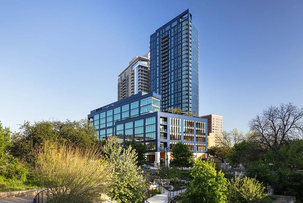 Stunning modern apartment building with sleek glass facade surrounded by lush greenery and a scenic walkway, perfect for urban living.