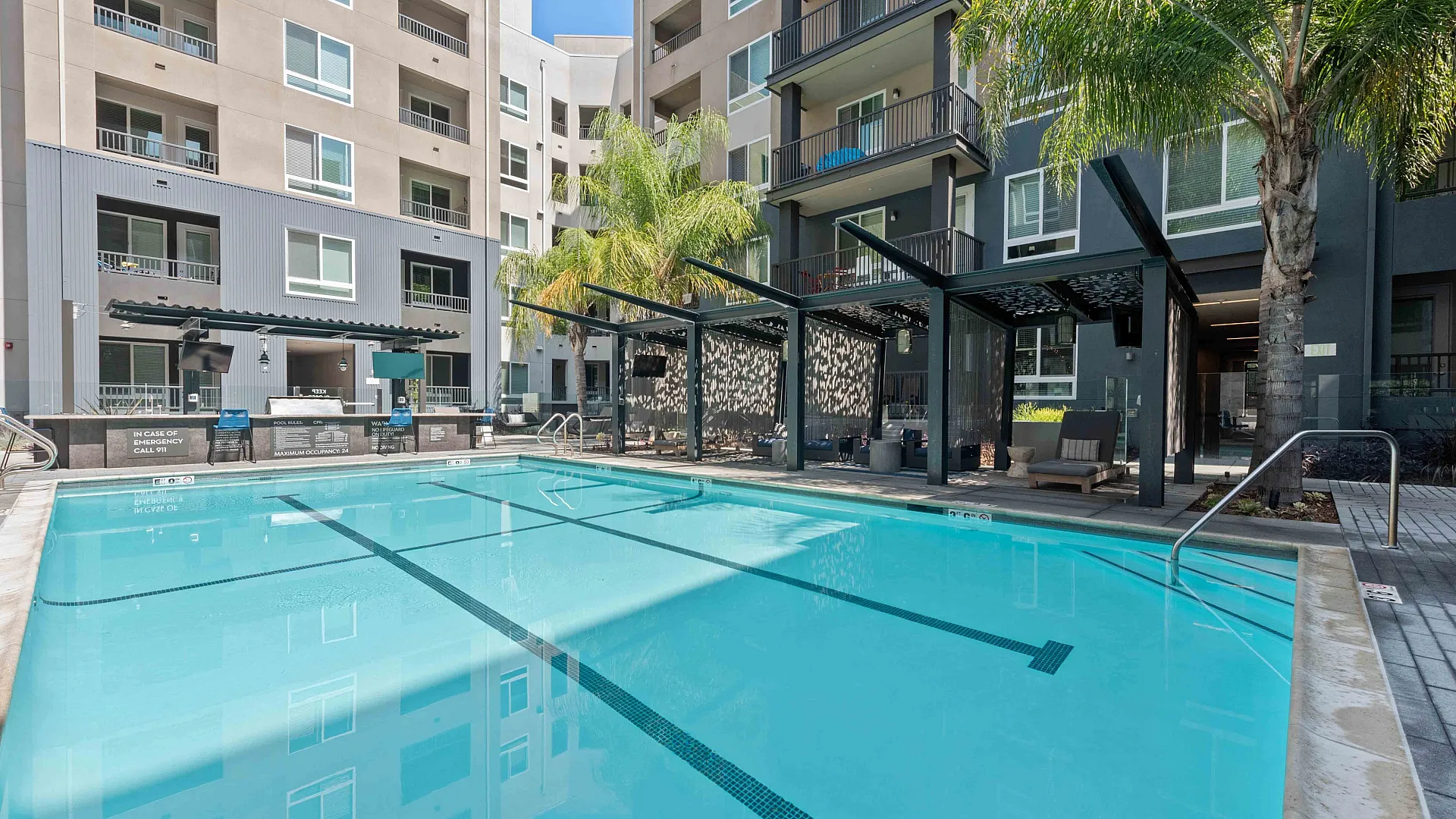 Modern apartment complex features a stylish outdoor pool area with a sleek barbecue station and comfortable seating.