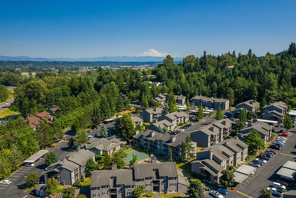 Breathtaking aerial view of a serene apartment community nestled in lush greenery with panoramic mountain backdrop.