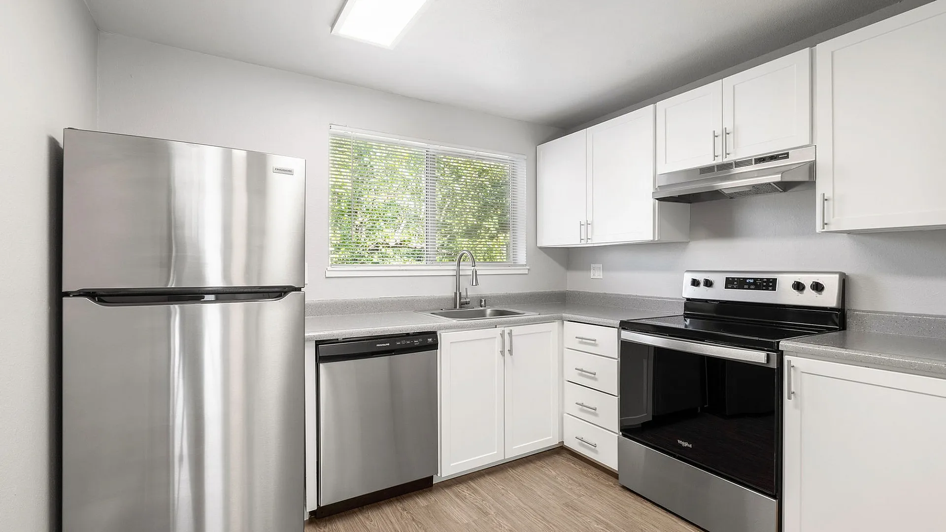 Modern kitchen with sleek stainless steel appliances, bright white cabinets, and elegant countertops, accentuated by natural light from a large window.