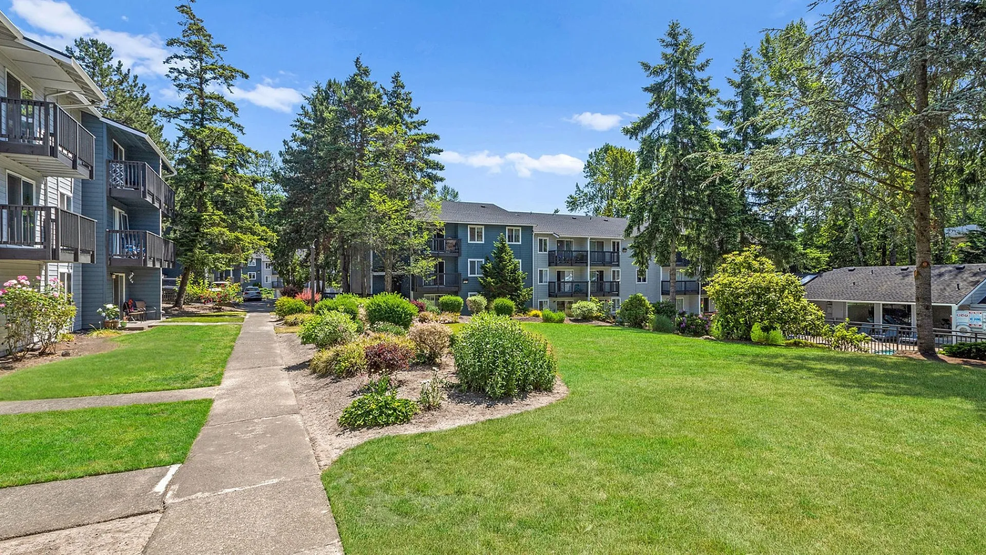 Charming apartment complex surrounded by lush greenery and vibrant gardens under a clear blue sky.