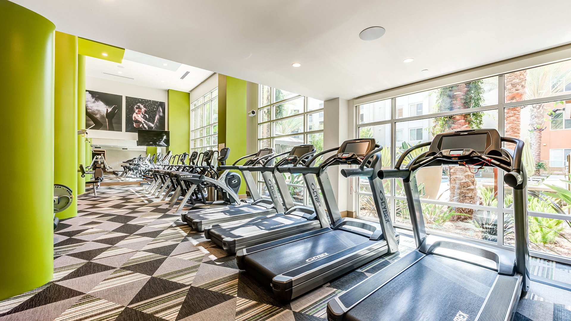 Bright and modern fitness center featuring sleek treadmills, vibrant green accents, and expansive windows with natural light.