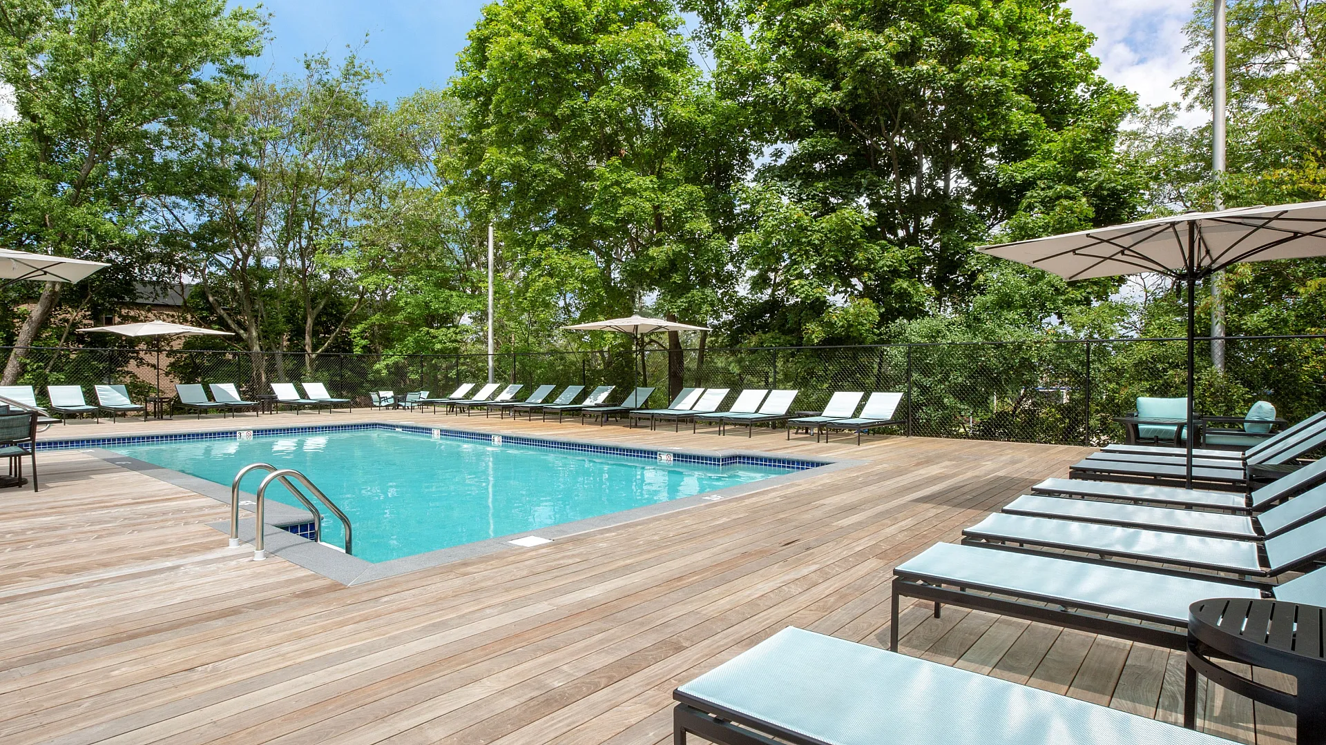 Inviting outdoor pool deck with elegant lounge chairs and umbrellas, surrounded by lush greenery.