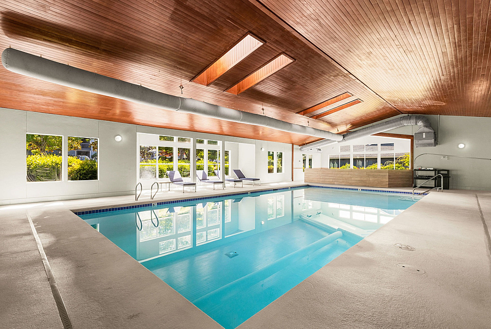 Bright and modern indoor pool area with sleek wooden ceilings and comfortable lounge chairs, perfect for relaxation and leisure.