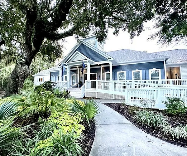 Inviting blue and white clubhouse nestled among lush greenery, featuring a welcoming entrance with a charming walkway.