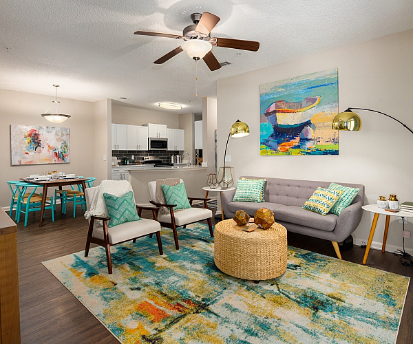 Charming open-concept living space with modern decor, featuring a cozy gray sofa, colorful artwork, elegant dining area, and well-equipped kitchen.