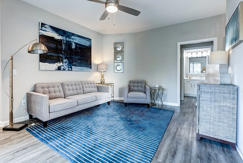 Elegant living room with modern decor, featuring a comfortable grey sofa, stylish armchair, and vibrant blue area rug. Bright and inviting with natural light and chic artwork.