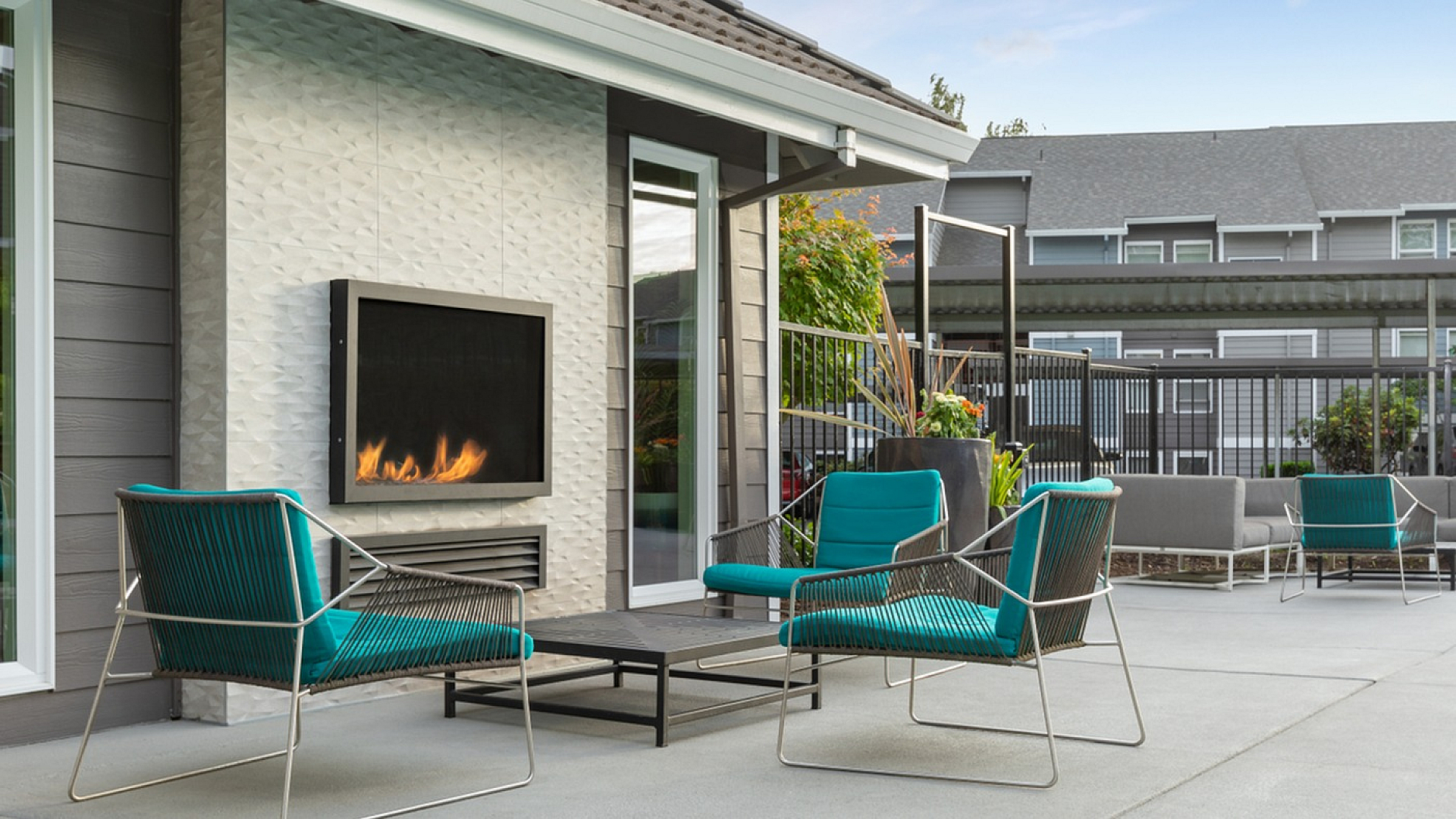 Modern outdoor patio with stylish turquoise seating, elegant fireplace, and lush greenery, ideal for relaxation and entertaining.