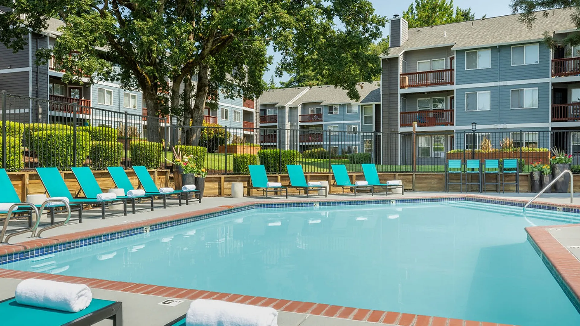 Luxurious apartment complex featuring a sparkling outdoor pool surrounded by vibrant greenery and comfortable lounge chairs.