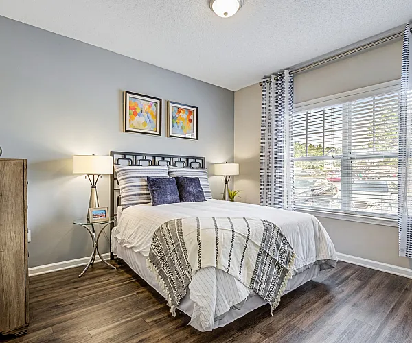 Charming and cozy bedroom featuring modern decor, wooden flooring, and ample natural light from large windows.