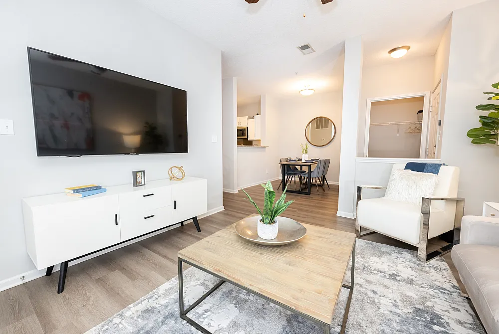 Modern living room with sleek furniture, large wall-mounted TV, and stylish decor leading to a cozy dining area with elegant lighting.
