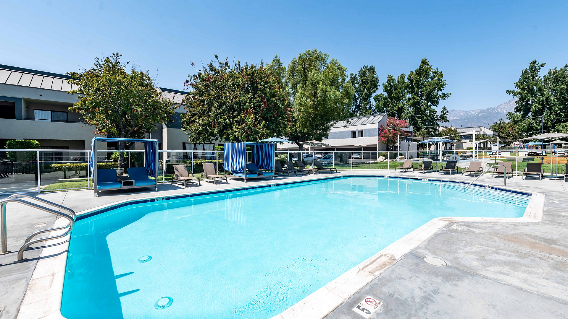 Luxurious apartment complex pool area at dusk, featuring inviting lounge chairs, a sparkling blue pool, and modern cabanas, perfect for relaxation and leisure.