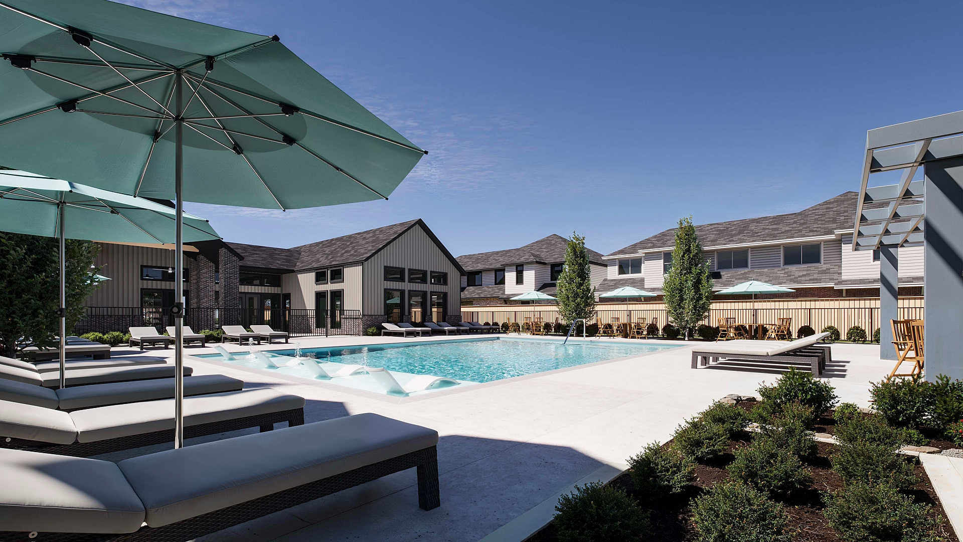 Luxurious apartment community featuring a pristine pool, surrounded by modern lounge chairs and stylish umbrellas, perfect for relaxation and entertainment.