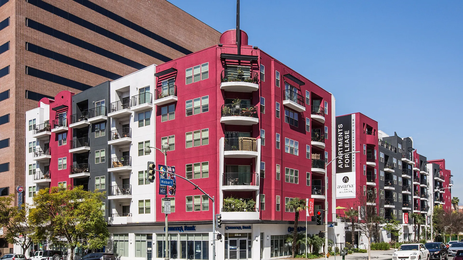 Contemporary urban apartment building with vibrant red and black facade, offering modern living spaces with private balconies in a bustling city setting.