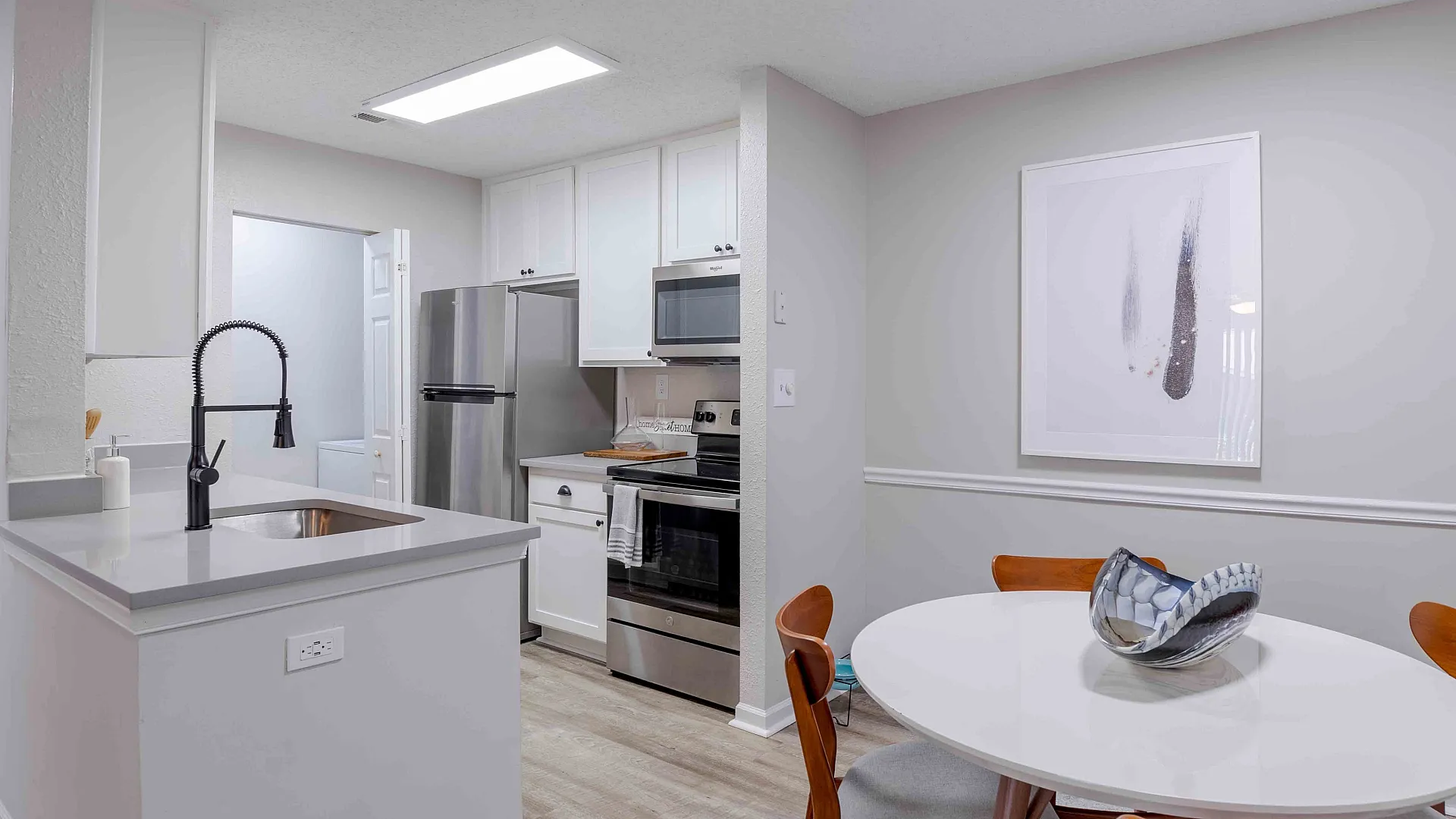 Modern kitchen with sleek stainless steel appliances and an elegant dining area, featuring a contemporary oval table with stylish wooden chairs.