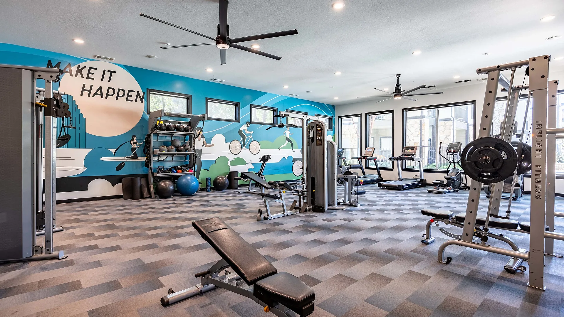 Modern gym with advanced cardio equipment, strength training machines, and ample free weights, set in a bright, spacious environment with ceiling fans and multiple TVs.