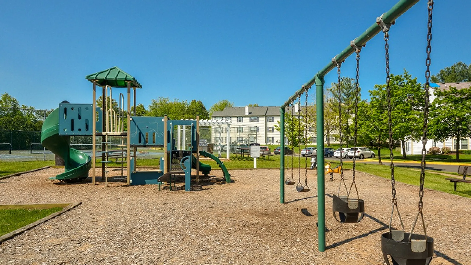Inviting outdoor playground with slides and swings, set against a backdrop of greenery and bright blue skies, perfect for family-friendly living.