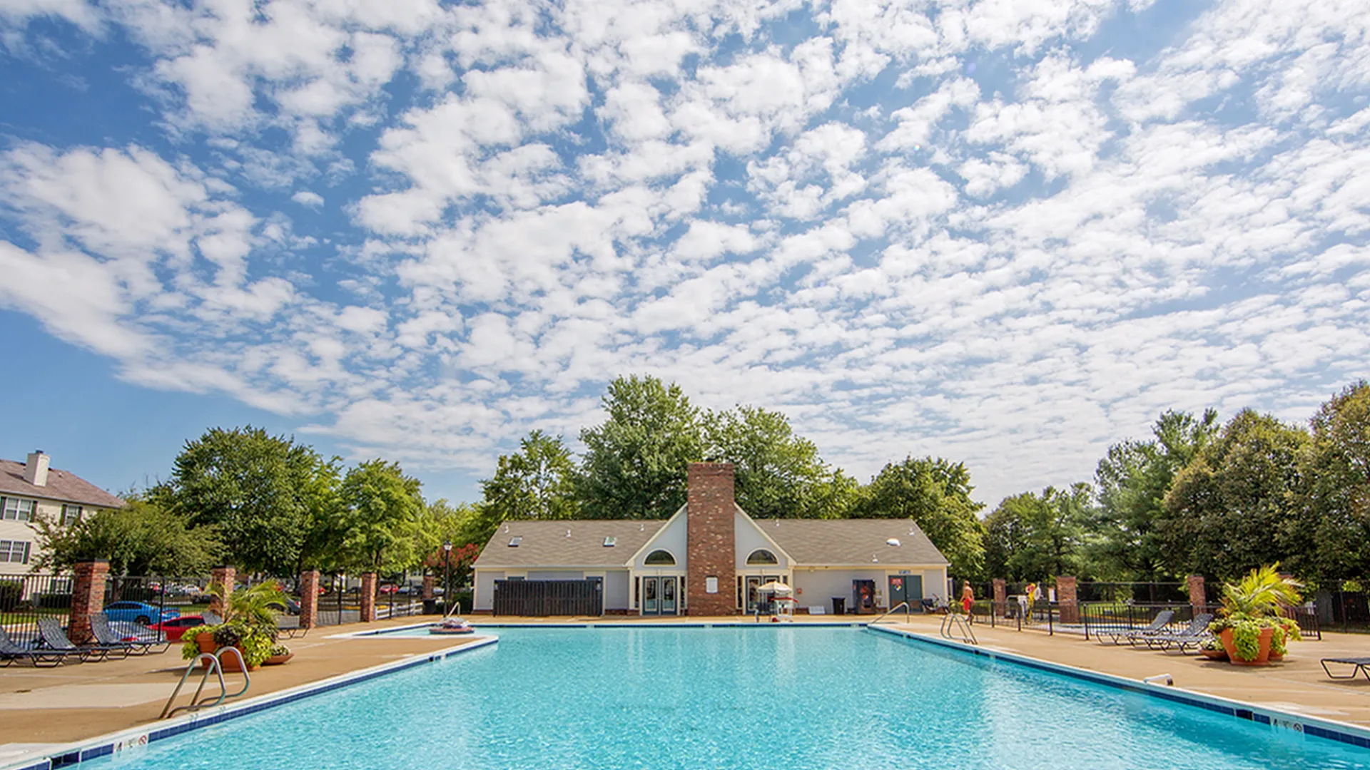 Inviting outdoor pool area with clear blue water, surrounded by lush greenery and comfortable lounge chairs, perfect for relaxation under a picturesque sky.