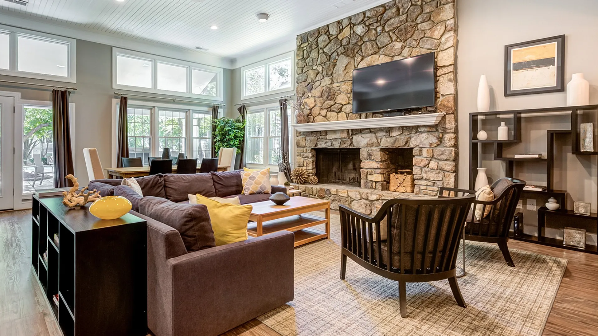 Inviting living room with large stone fireplace, elegant wood flooring, and abundant natural light from expansive windows.