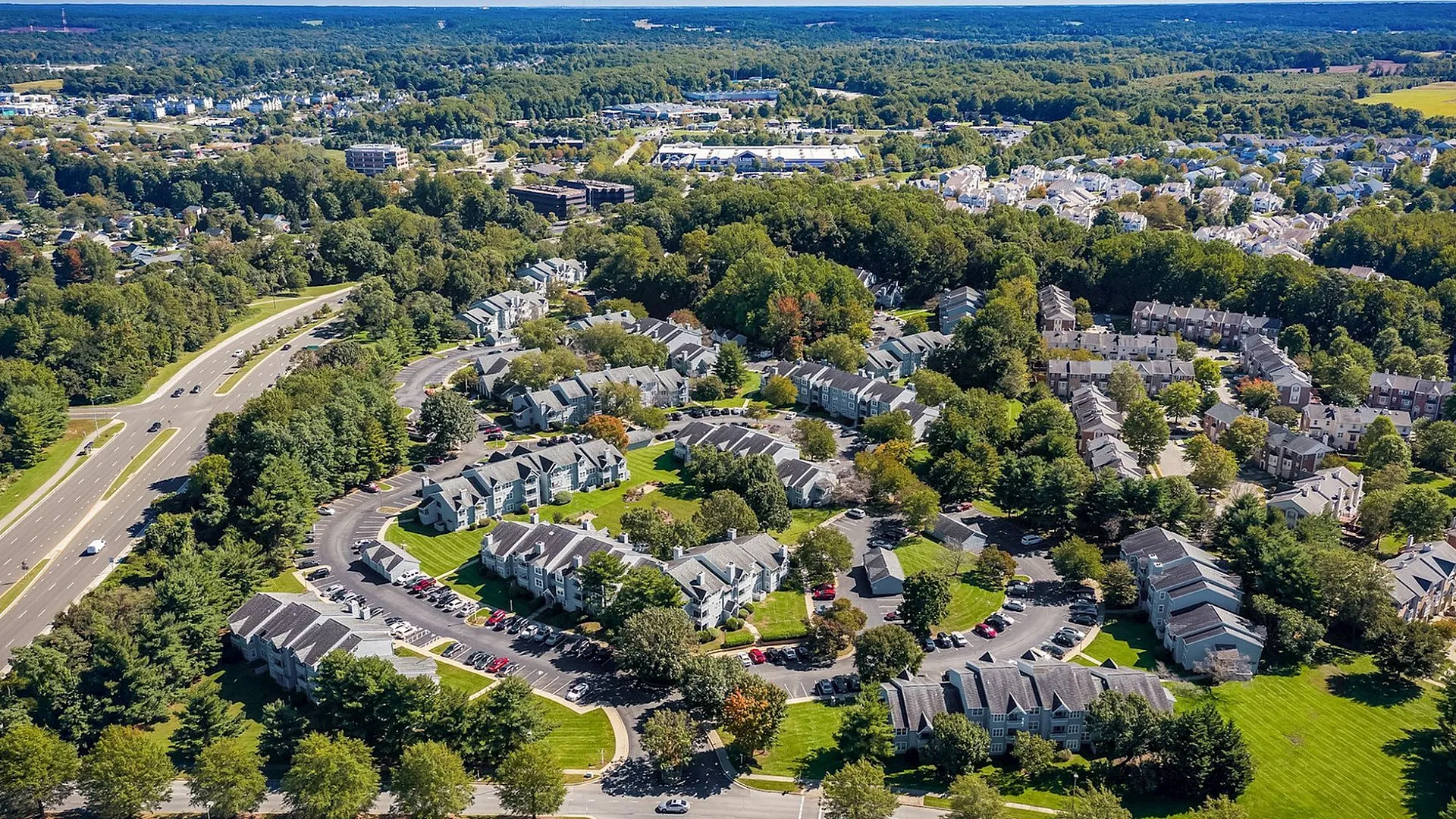 Aerial view of a charming residential community surrounded by lush greenery, featuring modern townhouses and well-maintained landscapes.