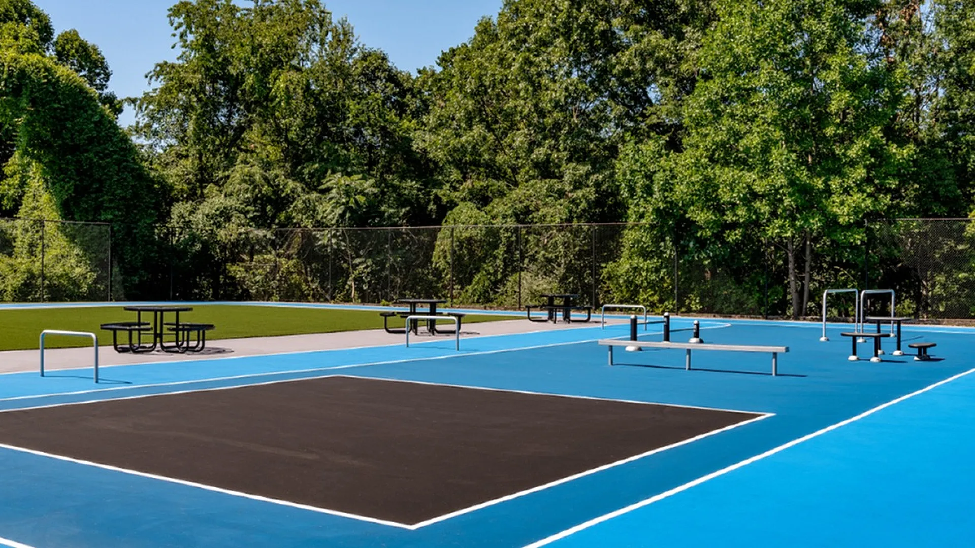 Vibrant outdoor sports complex featuring a modern, multi-functional court surrounded by lush greenery and picnic tables.