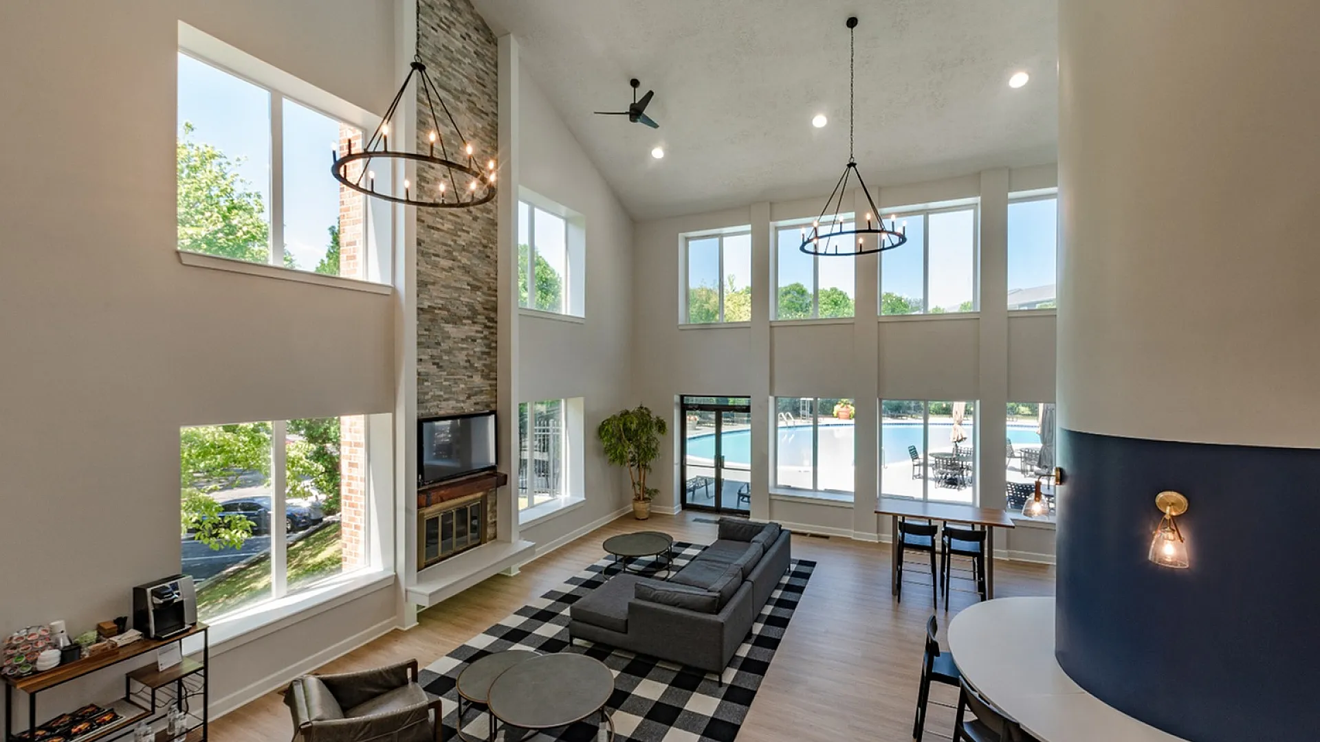 Elegant modern living space with high ceilings, large windows, and stylish chandeliers overlooking a sparkling pool, perfect for relaxation and social gatherings.