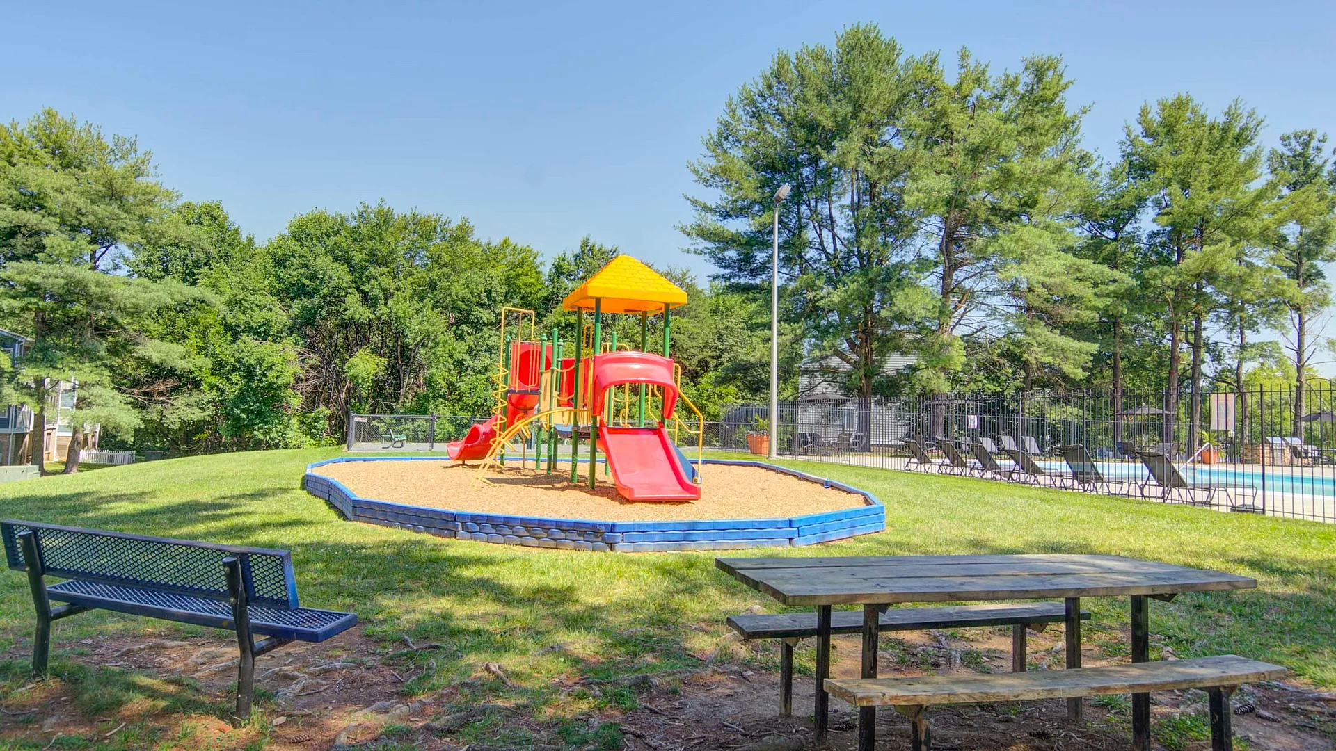 Inviting outdoor playground with vibrant equipment, surrounded by lush greenery and nearby poolside relaxation area.