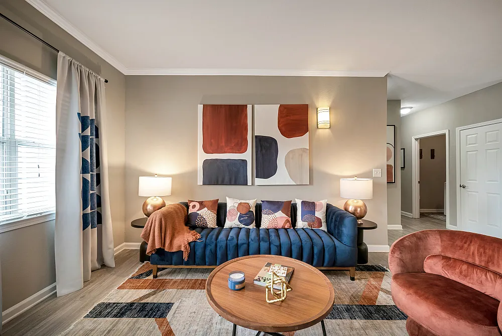 Chic living room with a plush blue sofa accented by colorful pillows, modern abstract art, and a cozy vibe highlighted by warm lighting and stylish decor.