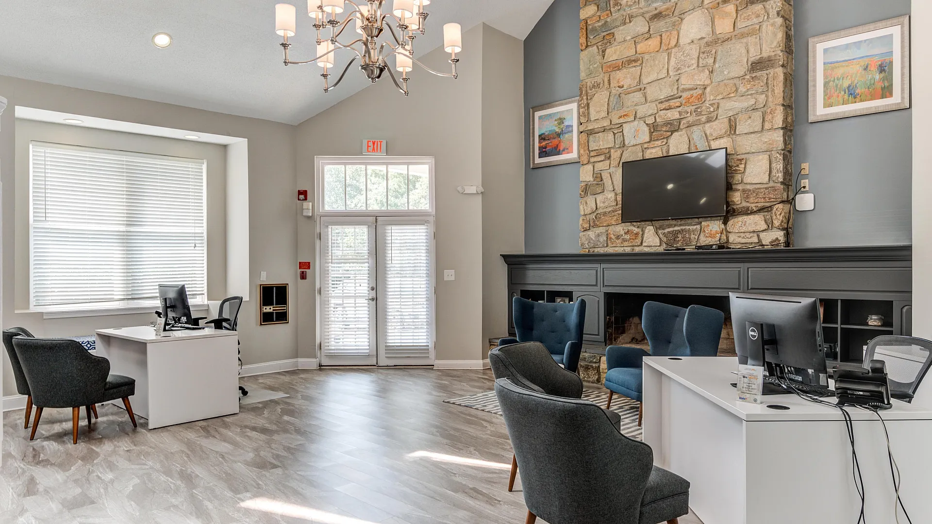 Chic office space with large stone fireplace, elegant chandelier, and modern furnishings under a vaulted ceiling.