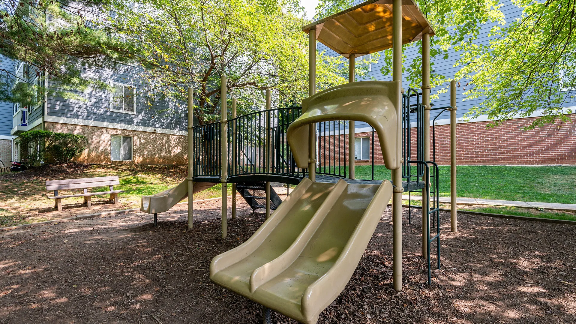 Charming playground with slides and climbing structure nestled under leafy trees, perfect for family enjoyment.
