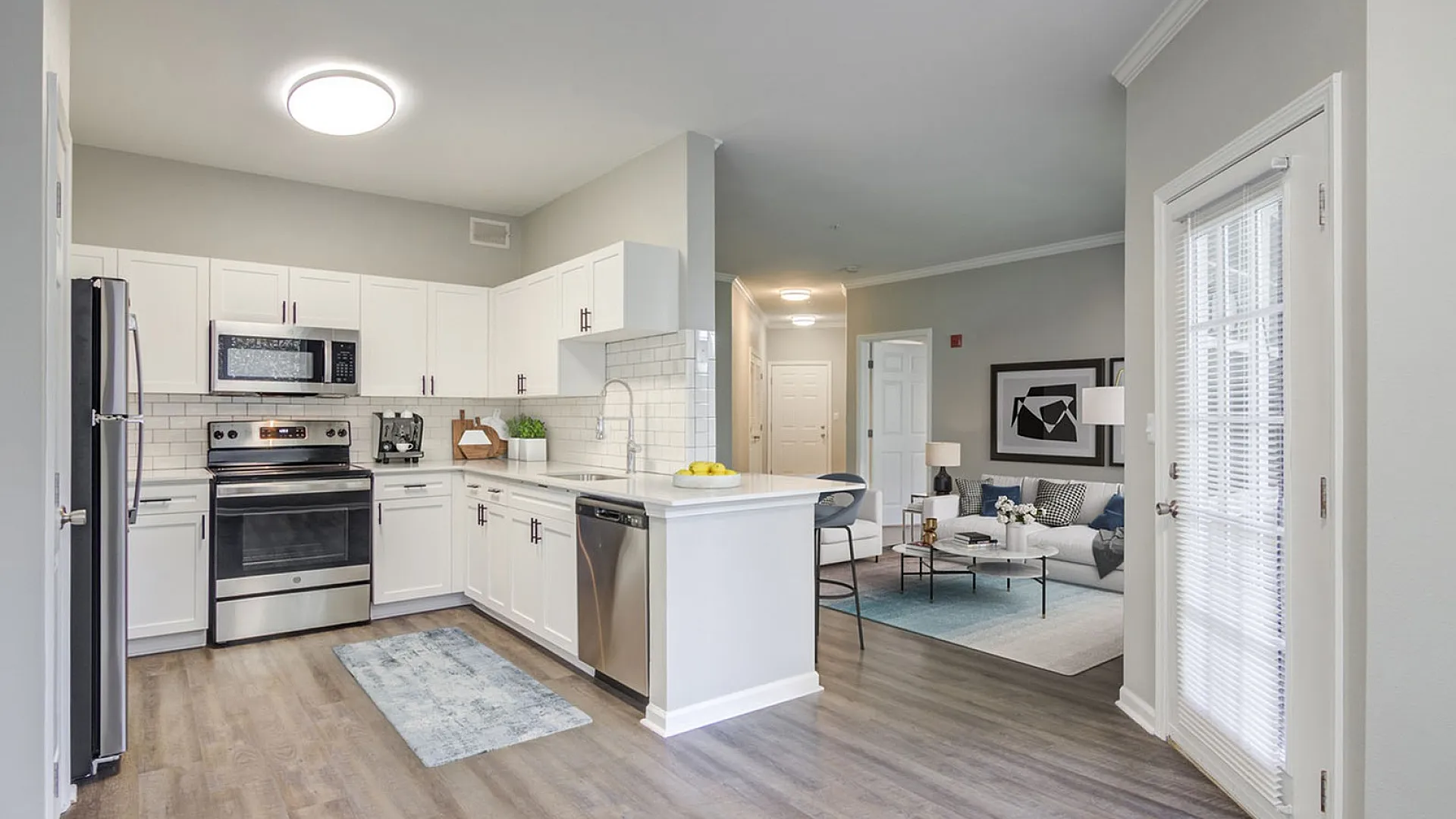 Modern open-concept kitchen with sleek stainless steel appliances, pristine white cabinetry, and cozy adjacent living area, perfect for comfortable living.