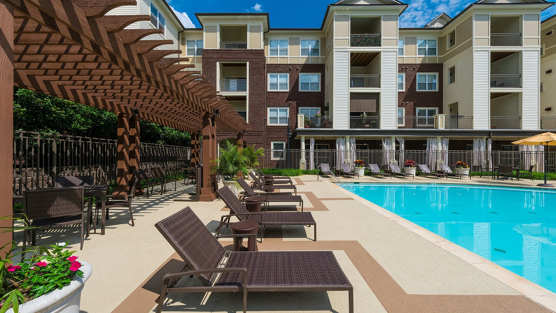Luxurious apartment complex with a vibrant swimming pool, stylish pergola, and inviting lounge chairs, set against a beautiful sunny backdrop.