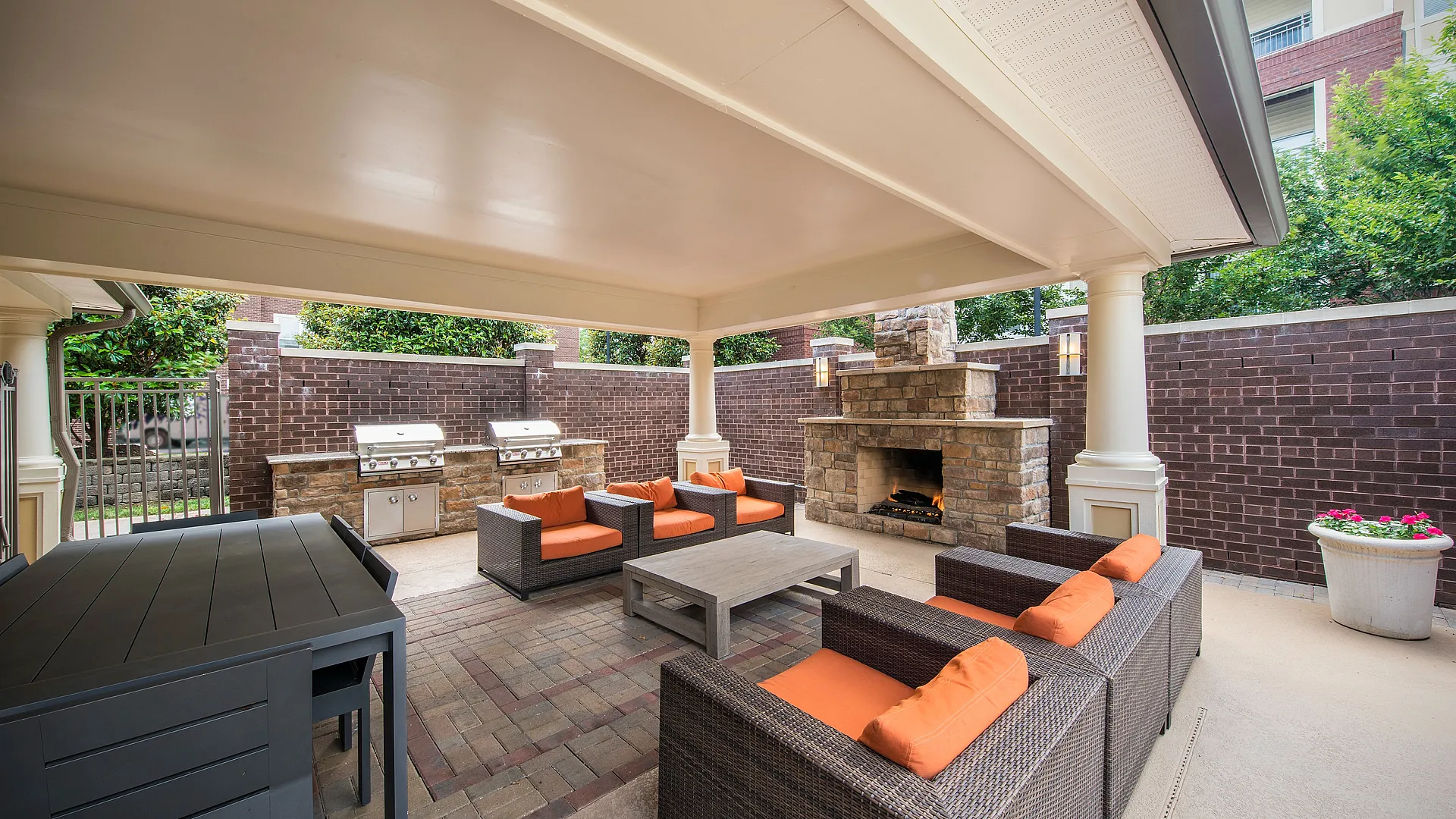 Elegant outdoor patio featuring cozy wicker seating with vibrant orange cushions, a modern fireplace, and dual stainless steel grills, creating a perfect ambiance for entertaining guests.